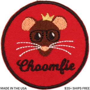 Könnte beinhalten: Ein runder, roter, gestickter Aufnäher mit einer Cartoon-Maus, die eine Brille und eine goldene Krone trägt. Die Maus hat braunes Fell, weiße Schnurrhaare und das Wort "Choomfie" in schwarzer Schrift. Der Aufnäher ist schwarz umrandet.