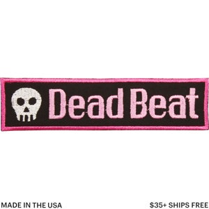 Könnte beinhalten: Rechteckiger, gestickter Aufnäher mit schwarzem Hintergrund und rosa Umrandung. Er zeigt einen weißen Totenkopf und die rosa Schriftzüge "Dead Beat". Der Aufnäher ist wahrscheinlich aus Stoff und zum Aufnähen oder Aufbügeln auf Kleidung oder Accessoires gedacht.