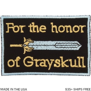 May include: Black rectangular patch with light blue border, featuring the text "For the honor of Grayskull" in gold lettering. A light blue sword with gold hilt is centered on the patch. Made in the USA.