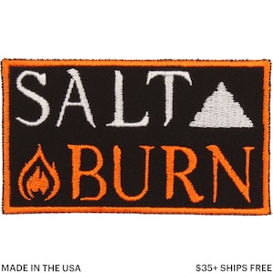 May include: A rectangular black patch with the words "SALT BURN" in white and orange lettering. A white triangle and orange flame graphic are also featured. The patch has an orange border.