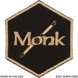 May include: Black and gold embroidered patch with the word "Monk" and crossed drumsticks. The patch is in a hexagonal shape with a gold border. The text "MADE IN THE USA" is at the bottom.