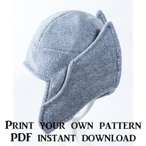 May include: A gray fleece hat with ear flaps. The hat is designed to cover the ears and neck for warmth. The text "PRINT YOUR OWN PATTERN PDF INSTANT DOWNLOAD" is at the bottom of the image.