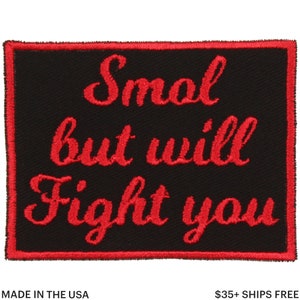 May include: Black rectangular patch with red embroidered text that reads "Smol but will Fight you." The patch has a red border and the text is in a cursive font. The words "MADE IN THE USA" are at the bottom.