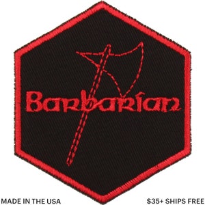 May include: Black hexagon patch with a red border and the word "Barbarian" in red script. A red axe graphic is stitched above the word. The patch is made in the USA.
