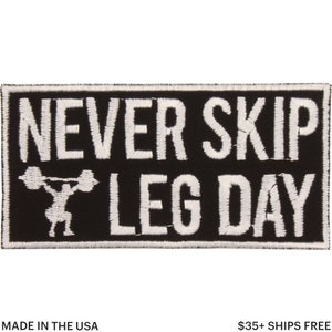 May include: Black rectangular patch with white embroidered text that reads "NEVER SKIP LEG DAY". A weightlifter graphic is below the words. The patch is made in the USA.