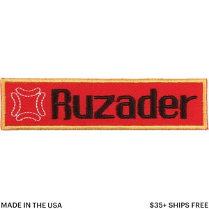May include: A rectangular red embroidered patch with the word "Ruzader" in black, and a white stitched design on the left. The patch has a gold border.