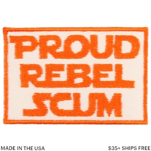 May include: Rectangular patch with the words "PROUD REBEL SCUM" in orange, embroidered on a white background. The patch has an orange border. The text is in a bold, sans-serif font. The words "MADE IN THE USA" are at the bottom.