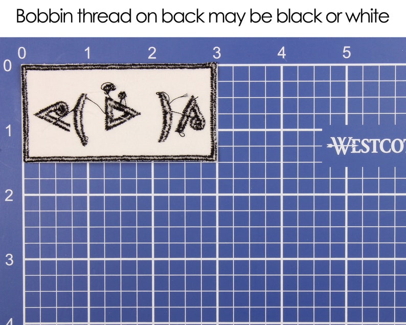 Pu&ograve; includere: Una toppa rettangolare con simboli ricamati neri su sfondo bianco. La toppa &egrave; bordata con cuciture nere. Il testo "Bobbin thread on back may be black or white" &egrave; sopra la toppa. La toppa &egrave; su una griglia blu.
