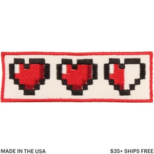 May include: Embroidered patch featuring three pixelated red hearts with black outlines, representing a health bar. The patch is rectangular with a red border and is on a white background. The text "MADE IN THE USA" is at the bottom.