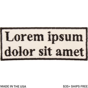 May include: A rectangular patch with the text "Lorem ipsum dolor sit amet" embroidered in black on an off-white background. The patch has a black border and the text "MADE IN THE USA" is at the bottom.