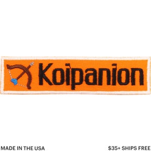 Puede incluir: Parche rectangular naranja con la palabra "Koipanion" en letras negras. Un arco y una flecha marrones con una flecha azul en forma de corazón están en el lado izquierdo. El parche tiene un borde blanco.