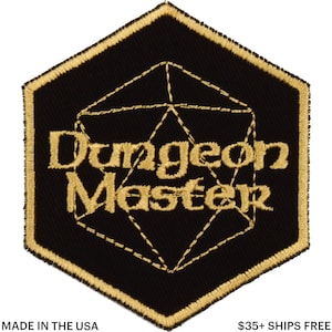 Könnte beinhalten: Schwarz-goldener, gestickter Aufnäher mit den Worten "Dungeon Master" und einer geometrischen Form. Der Aufnäher hat einen goldenen Rand und eine sechseckige Form. Der Text "MADE IN THE USA" steht unten.