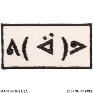 Pu&ograve; includere: Toppa rettangolare con sfondo bianco e disegno ricamato nero. Il disegno presenta simboli e forme astratte. La toppa ha un bordo nero e il testo "MADE IN THE USA" &egrave; in basso.
