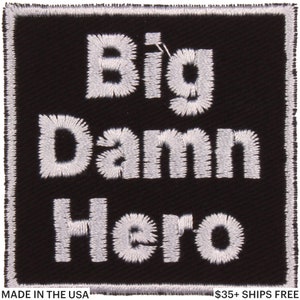 May include: Square black patch with white embroidered text reading "Big Damn Hero." The patch has a white border and the words are in a bold, sans-serif font. The phrase is centered on the patch.