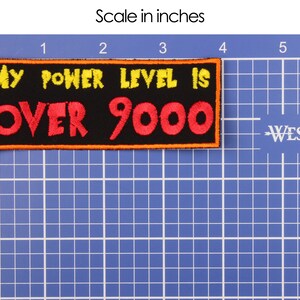 May include: A black rectangular patch with the text "MY POWER LEVEL IS OVER 9000" in yellow and red, with an orange border. The patch is approximately 4 inches long and 1.5 inches tall.