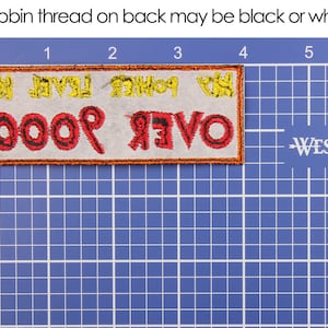May include: Embroidered patch with the text "OVER 9000" in red and black thread, with yellow text above. The patch is rectangular with an orange border, set against a blue grid. Text at the top reads "Bobbin thread on back may be black or white."
