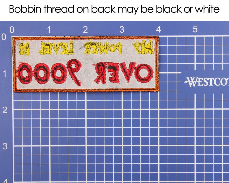 May include: Embroidered patch with the text "OVER 9000" in red and black thread, with yellow text above. The patch is rectangular with an orange border, set against a blue grid. Text at the top reads "Bobbin thread on back may be black or white."