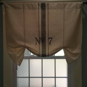 May include: A white window curtain with a black and white striped pattern and the text "No. 7" printed on it. The curtain is gathered at the sides and hangs over a window with frosted glass panes.