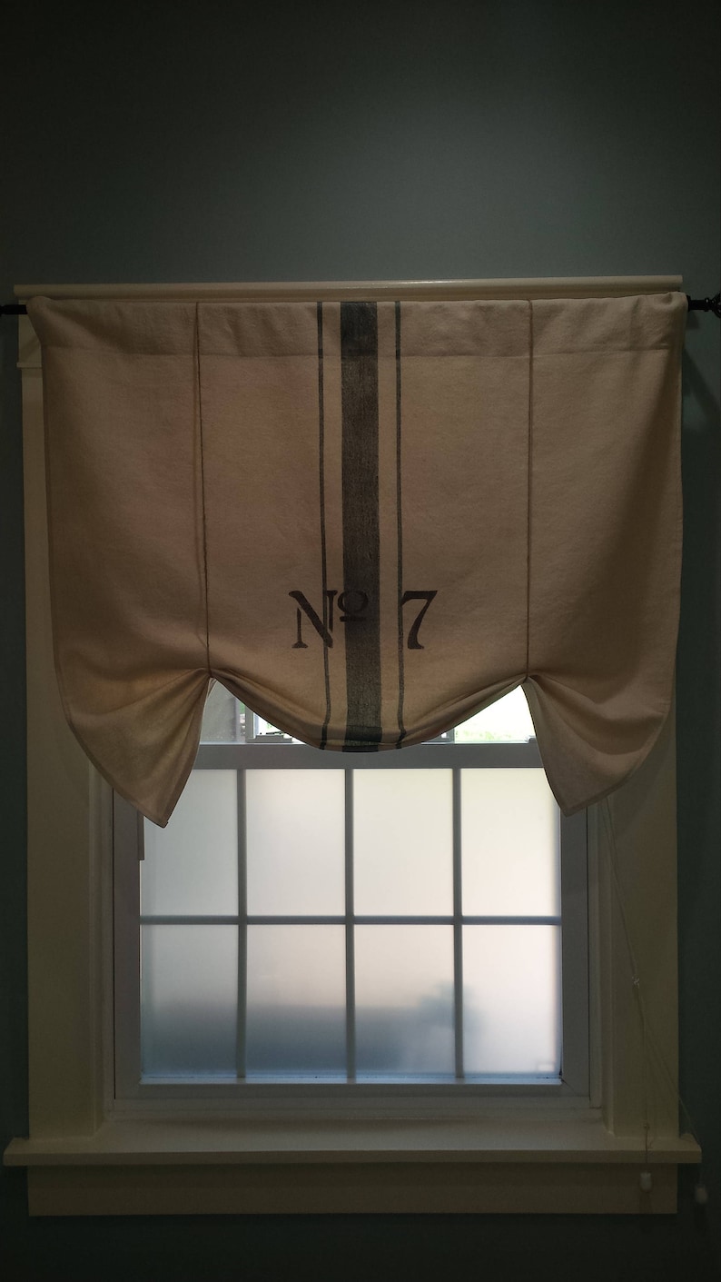 May include: A white window curtain with a black and white striped pattern and the text "No. 7" printed on it. The curtain is gathered at the sides and hangs over a window with frosted glass panes.