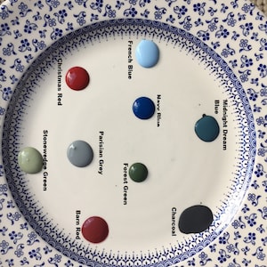 May include: A white plate with paint samples in various colors, including blue, green, red, and gray. The paint colors are labeled with names like "Midnight Dream Blue", "Navy Blue", "Forest Green", "Parisian Grey", "Christmas Red", "Stonewedge Green", "Charcoal", and "Barn Red".