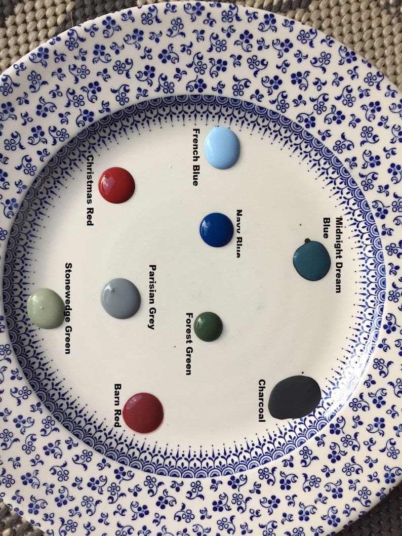 May include: A white plate with paint samples in various colors, including blue, green, red, and gray. The paint colors are labeled with names like "Midnight Dream Blue", "Navy Blue", "Forest Green", "Parisian Grey", "Christmas Red", "Stonewedge Green", "Charcoal", and "Barn Red".