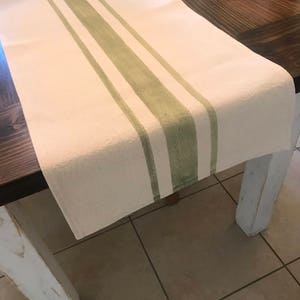 May include: A white table runner with green stripes. The runner is on a wooden table with a white painted leg.