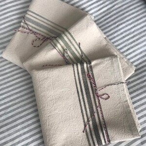 May include: Three white linen tea towels with different colored stripes. The towels are folded and tied with twine.