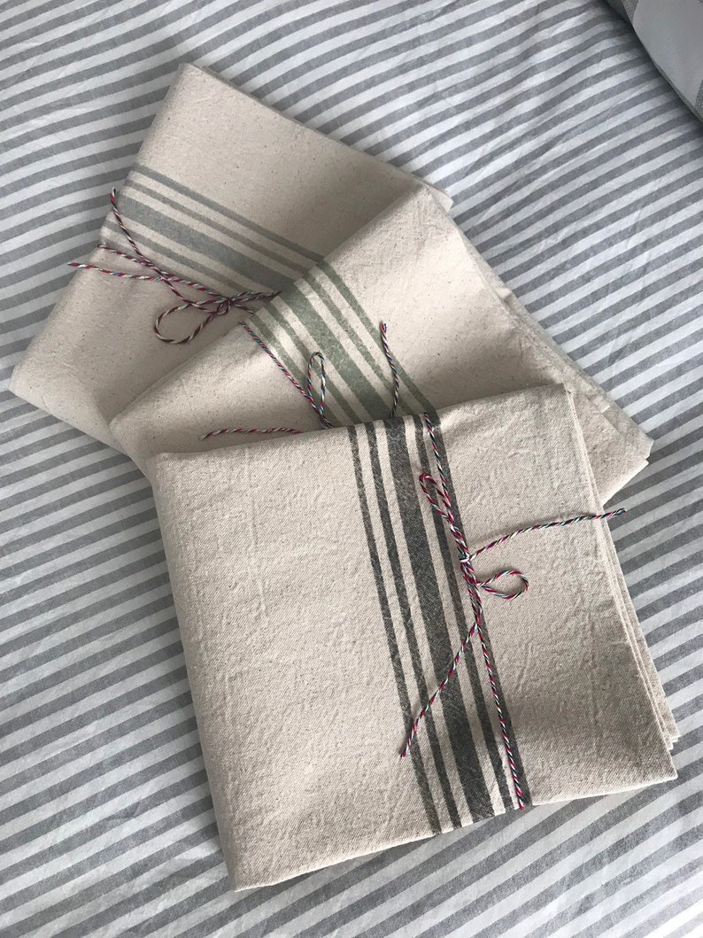 May include: Three white linen tea towels with different colored stripes. The towels are folded and tied with twine.