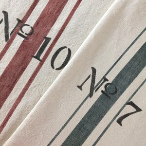 May include: Two white tea towels with red and blue stripes. The top towel has the text "No. 10" and the bottom towel has the text "No. 7".