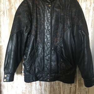 Peut inclure: Veste en cuir noir avec une section supérieure à motif peau de serpent. La veste a un col montant, des boutons et deux poches avant. Les manches ont des poignets boutonnés et la taille est élastiquée.