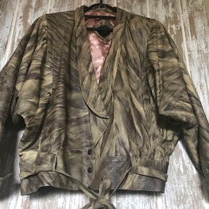 May include: A vintage brown leather jacket with a unique, swirled pattern. The jacket features a shawl collar, button closure, and a tie belt. The interior lining is a soft pink color. The jacket has a retro, oversized silhouette.