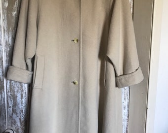 May include: A beige, knee-length coat with a stand-up collar and three buttons down the front. The coat has long sleeves with folded cuffs and two pockets. The coat is made of a soft, wool-like material.