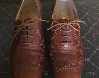 May include: A pair of brown leather oxford shoes with brogue detailing. The shoes feature a classic lace-up design and a polished finish. The soles are black, and the shoes appear to be in good condition.