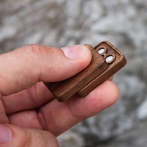 May include: A small wooden box with a hinged lid. The box has two circular openings on the top.
