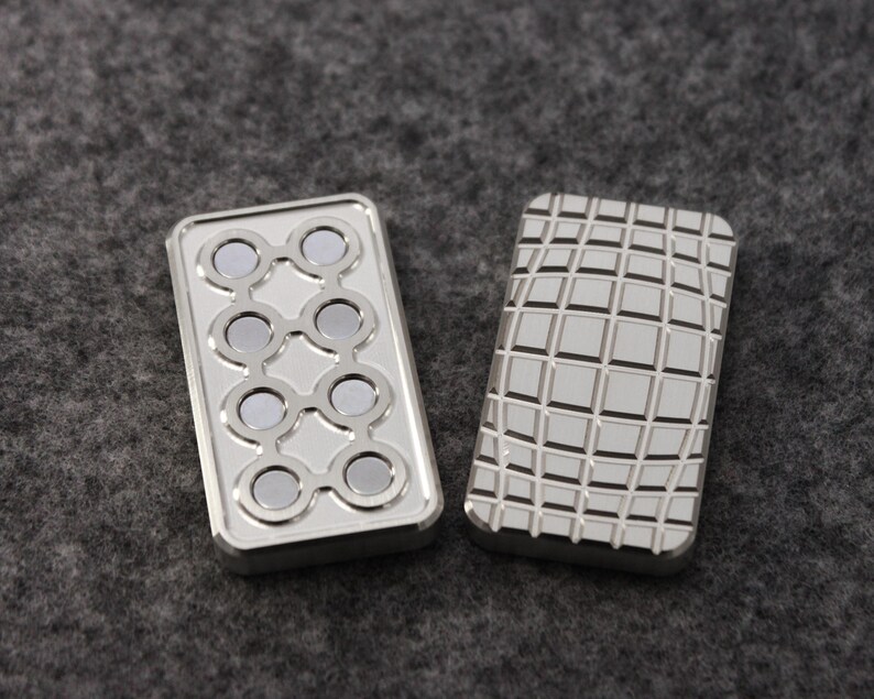 May include: Two silver rectangular fidget toys. One has a pattern of eight circular magnets, and the other has a grid pattern. The toys are displayed on a gray surface.