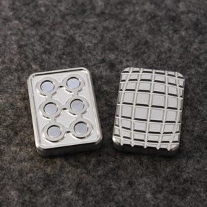 May include: Two silver metal fidget toys. One has six circular magnets arranged in a pattern. The other has a grid pattern. Both are rectangular and have a shiny finish. The background is a textured gray surface.