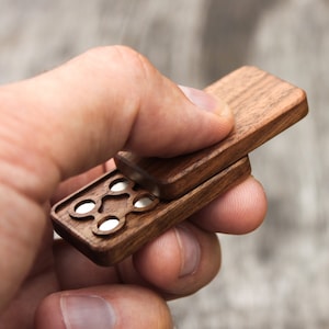 May include: A wooden box with a hinged lid, revealing a series of small, round, silver-colored compartments. The box is made of dark wood with a smooth finish.