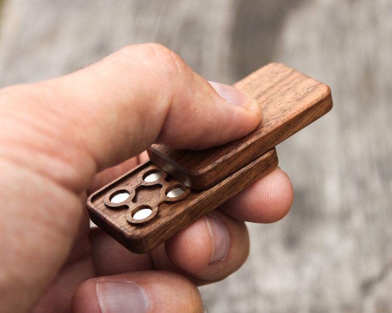 May include: A wooden box with a hinged lid, revealing a series of small, round, silver-colored compartments. The box is made of dark wood with a smooth finish.