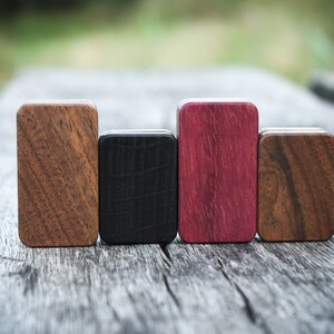 May include: Four small wooden boxes in different wood types and colors. The boxes are arranged in a row from left to right: brown, black, purple, and brown.