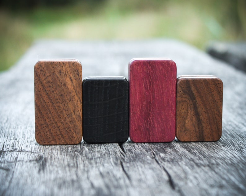 May include: Four small wooden boxes in different wood types and colors. The boxes are arranged in a row from left to right: brown, black, purple, and brown.