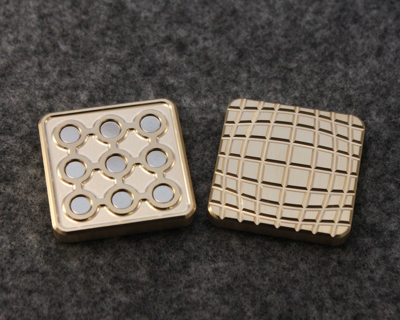 May include: Two square, gold-colored fidget toys. One has nine silver magnets arranged in a grid, the other has a textured, grid-like pattern. The toys are designed to be manipulated and provide a tactile experience.