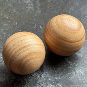 May include: Two wooden spheres with a light brown color and visible wood grain. The spheres are smooth and round, with a natural finish. The spheres are likely decorative objects or components for crafts.