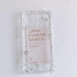 May include: Clear phone case with a decorative design. The case features the text "WAYS THANK YOU SO MUCH HAVE A NICE DAY" with star and planet embellishments. The case is made of clear plastic.
