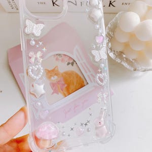 May include: Clear phone case with decorative embellishments. Features a pink cat illustration with a bow, bows, stars, hearts, and a mushroom. The text "Just for you" is visible on the case.