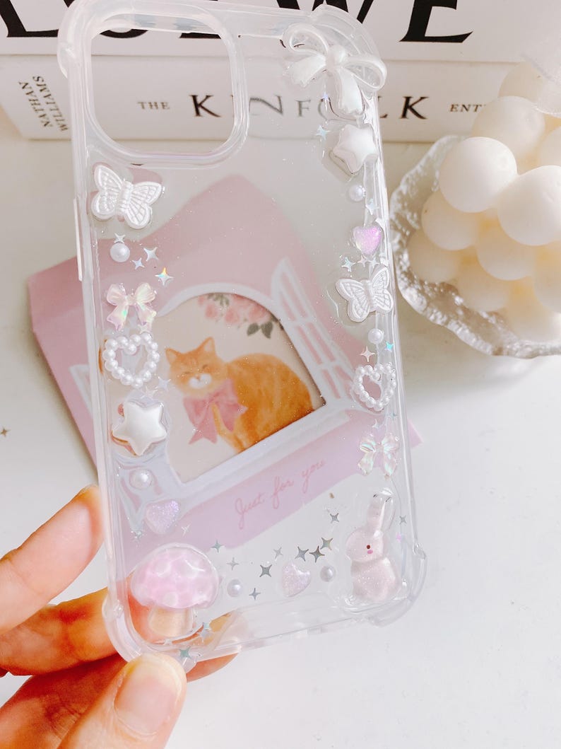 May include: Clear phone case with decorative embellishments. Features a pink cat illustration with a bow, bows, stars, hearts, and a mushroom. The text "Just for you" is visible on the case.