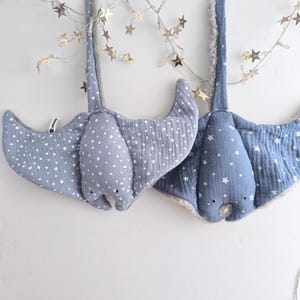 May include: Two plush stingray-shaped baby mobiles in shades of blue. One is patterned with white polka dots, the other with white stars. Both have a soft, fluffy trim and are suspended from a white surface.