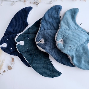 Puede incluir: Cuatro baberos de bebé de pana en tonos azules, dispuestos sobre una superficie blanca. Cada babero tiene forma de manta raya, con detalles blancos y pequeños ojos negros. Los baberos tienen una textura suave y afelpada.