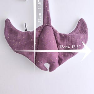 May include: A purple stuffed stingray toy with gold speckles, measuring 12.5 inches wide and 14.5 inches long. The toy has a white underside and is hanging against a white background. The toy is a children's item.