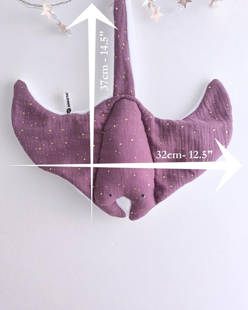 May include: A purple stuffed stingray toy with gold speckles, measuring 12.5 inches wide and 14.5 inches long. The toy has a white underside and is hanging against a white background. The toy is a children's item.