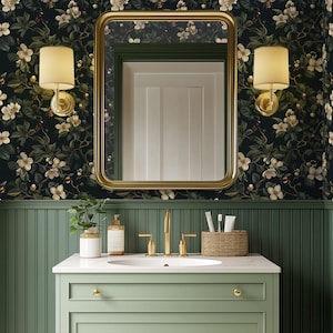 May include: A bathroom scene featuring a sage green vanity with a white countertop, gold fixtures, and a rectangular gold-framed mirror. The walls are adorned with floral wallpaper in dark green and cream tones. Two sconces with cream-colored shades flank the mirror.